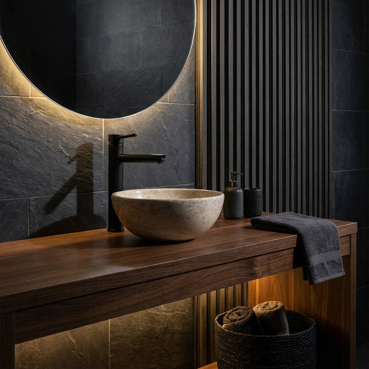 Lavabo sobre encimera redondo de piedra natural clara sobre un lavabo de madera oscura con grifería negra en un ambiente de baño elegante