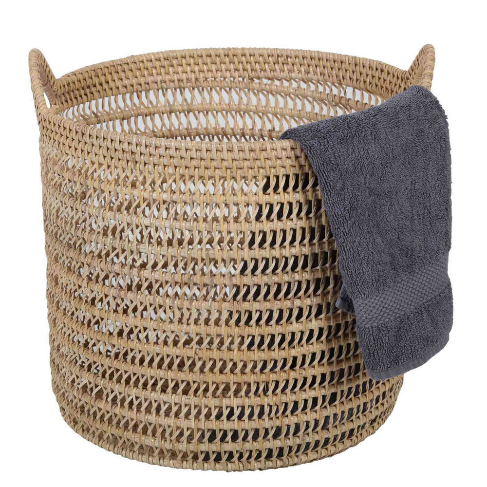 Cesta Eda de ratán en color natural con trenzado abierto, dos asas y una toalla gris oscuro sobre el borde.