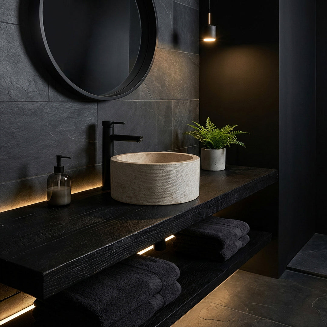 Lavabo sobre encimera redondo con elegante apariencia de mármol sobre una consola de madera oscura, en un baño minimalista de ambiente oscuro.