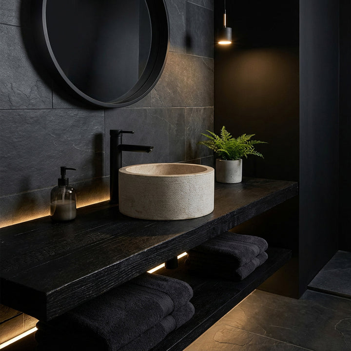Lavabo sobre encimera redondo con elegante apariencia de mármol sobre una consola de madera oscura, en un baño minimalista de ambiente oscuro.