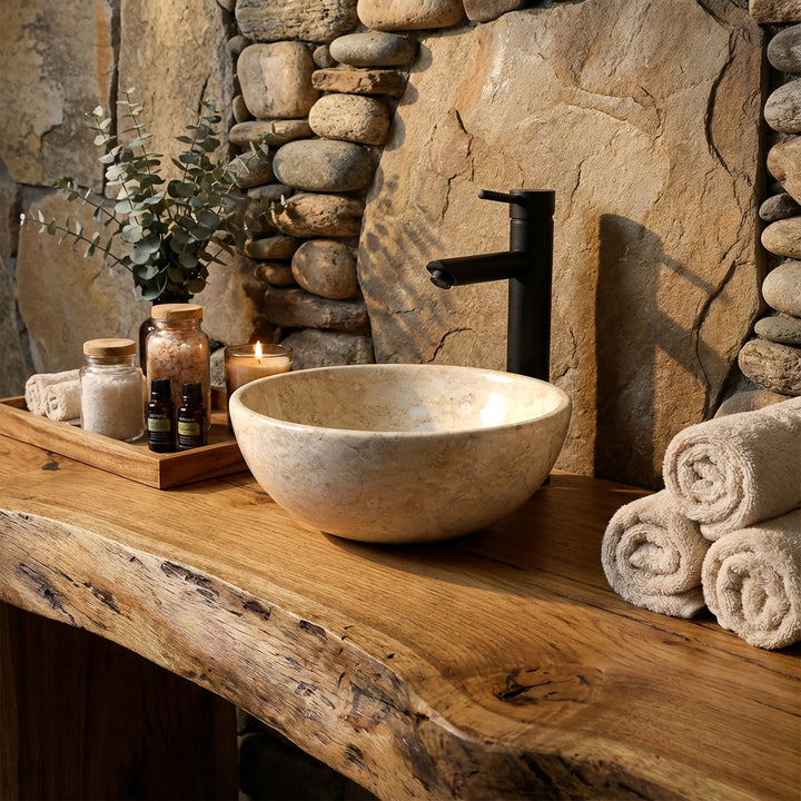 Lavabo de piedra clara como accesorio sobre una consola de madera maciza con grifería negra en un ambiente de baño spa natural