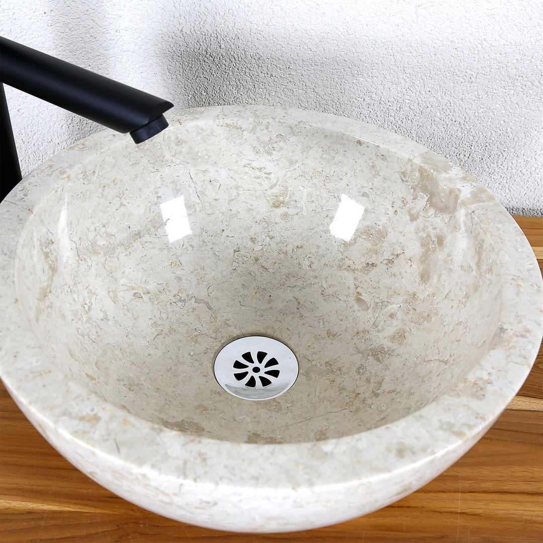 Vista detallada de un lavabo sobre encimera redondo fabricado en piedra natural clara con superficie interior pulida y desagüe central