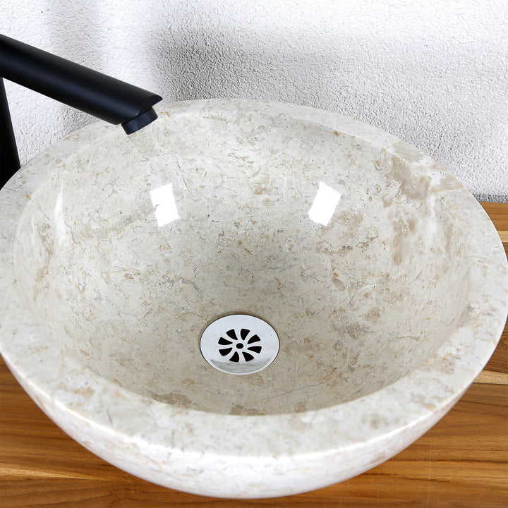 Vista detallada de un lavabo sobre encimera redondo fabricado en piedra natural clara con superficie interior pulida y desagüe central