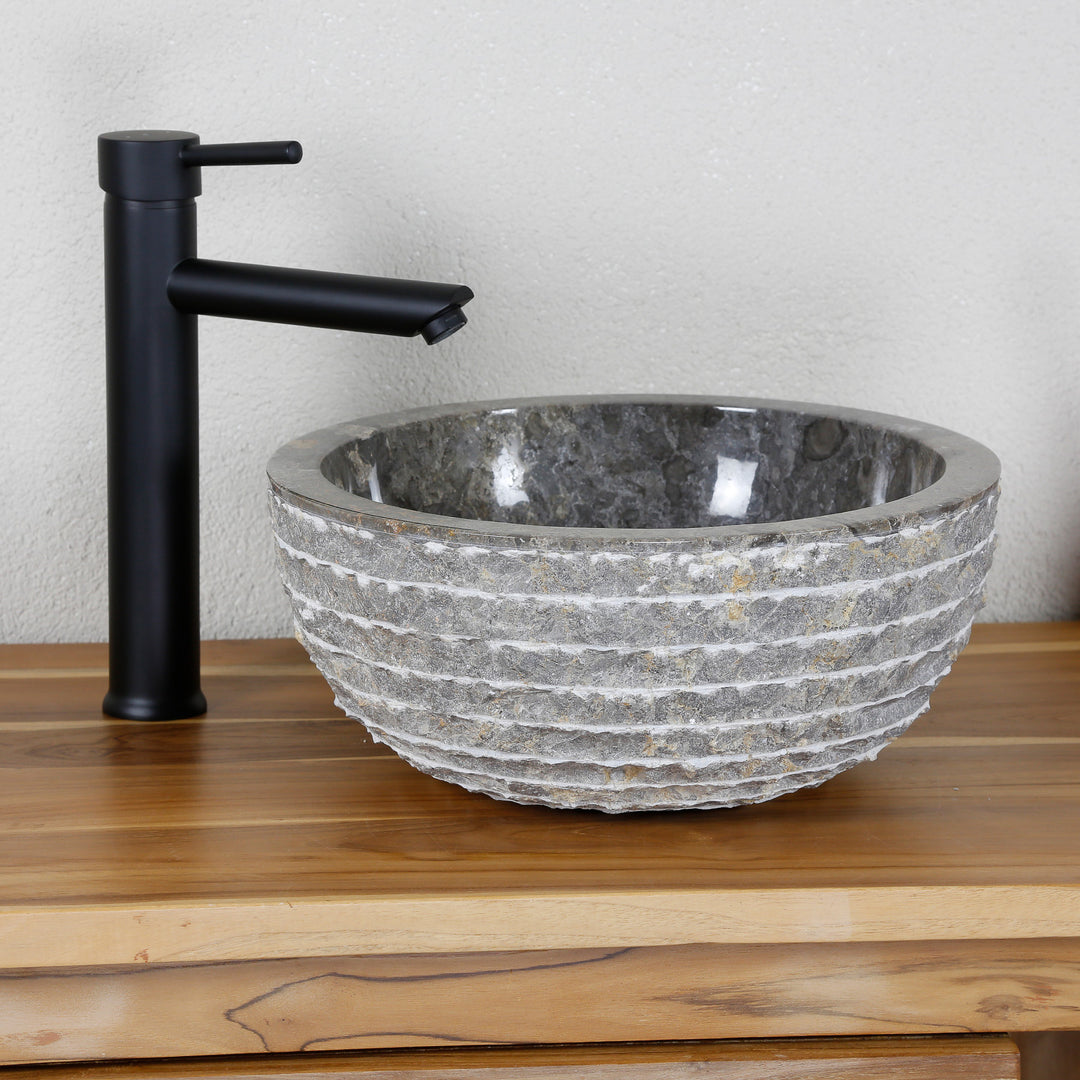 Lavabo sobre encimera redondo de piedra natural con superficie estructurada sobre tapa de madera, combinado con grifo independiente negro