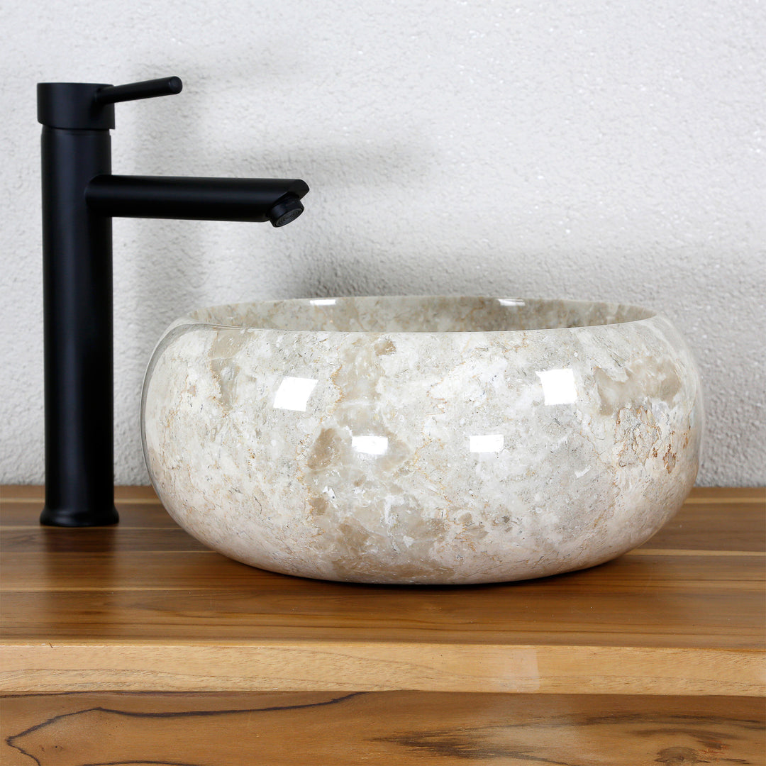 Lavabo sobre encimera redondo hecho de piedra natural clara sobre una tapa de madera con un accesorio negro en un ambiente de estudio neutro