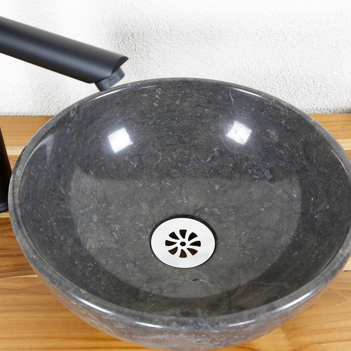 Lavabo sobre encimera redondo de piedra natural al detalle con superficie interior pulida, desagüe y grifería de acero inoxidable