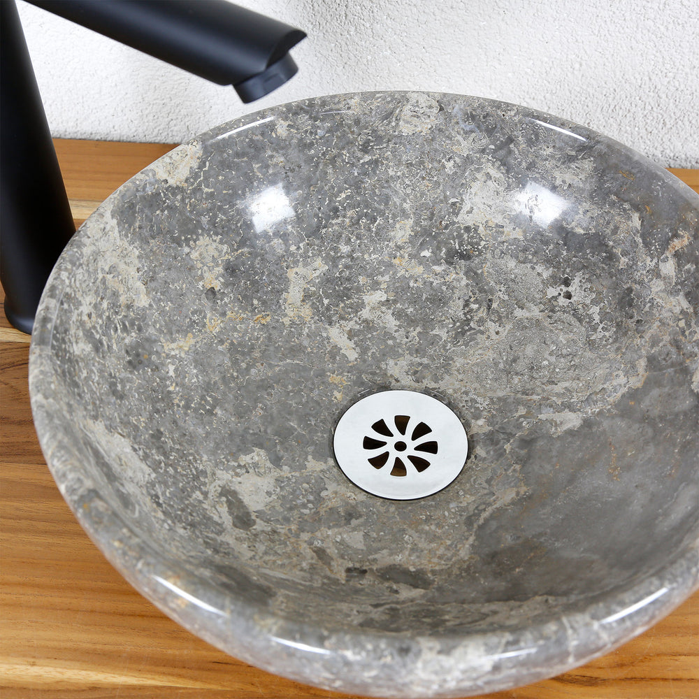 Vista del lavabo sobre encimera de piedra natural con veta marrón grisáceo y tapa de desagüe de acero inoxidable, combinado con un grifo independiente negro