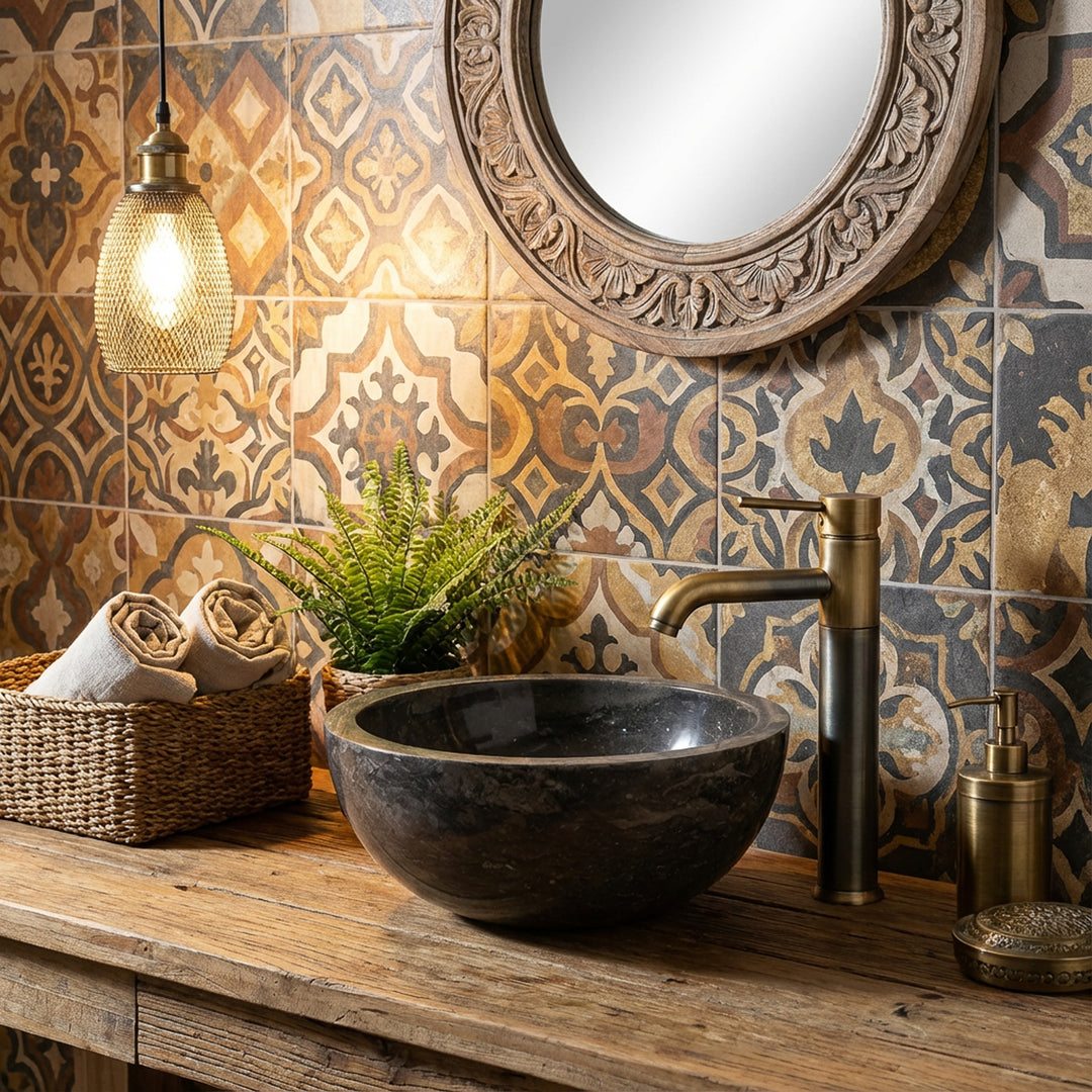 Rundes Aufsatzbecken aus Stein auf Holzwaschtisch mit Messingarmatur vor gemusterten Fliesen im warmen Badambiente