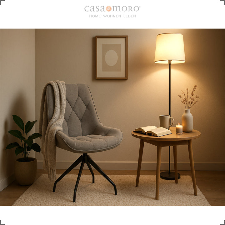 Grauer Esszimmerstuhl mit 360° Drehfunktion und schwarzem Metallgestell – gemütliche Leseecke mit Beistelltisch, Decke und warmem Licht