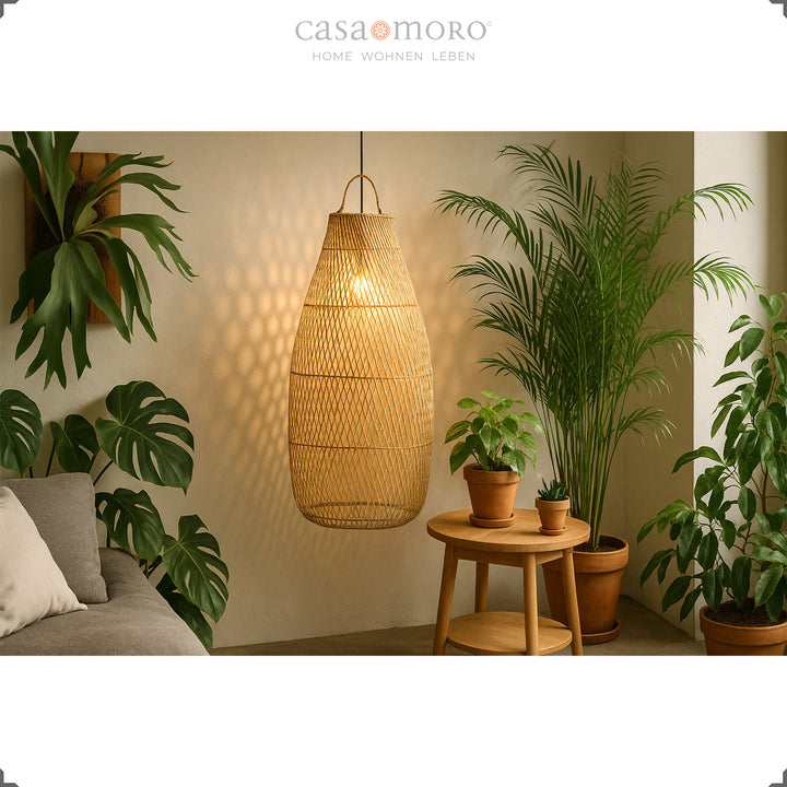 Hohe, hängende Rattanlampe im Wohnzimmer mit vielen Grünpflanzen und sanftem Licht