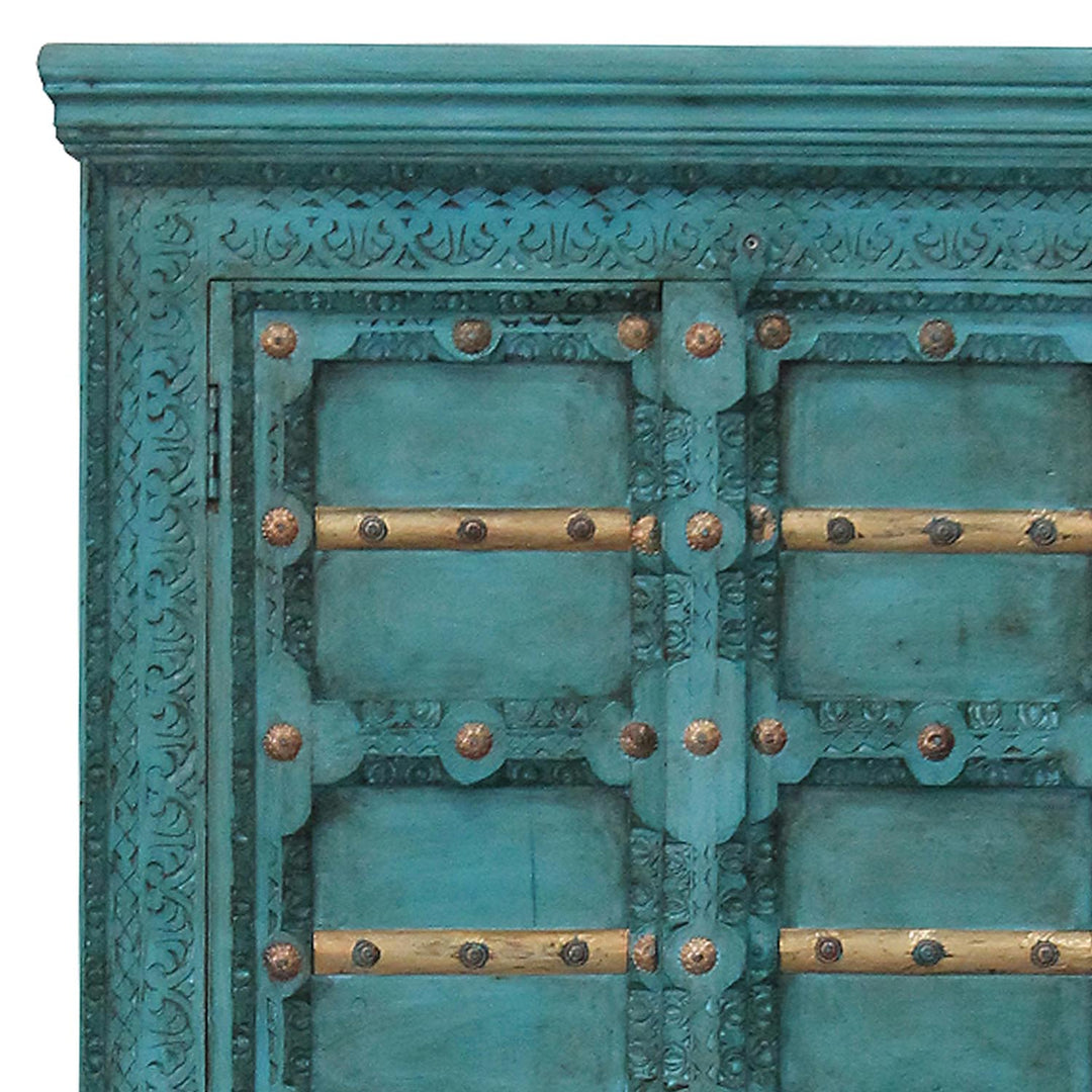 Detalle de las tallas ornamentales turquesas, los travesaños dorados y los herrajes de las puertas del armario.