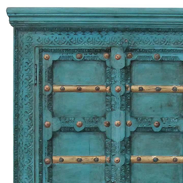 Detalle de las tallas ornamentales turquesas, los travesaños dorados y los herrajes de las puertas del armario.