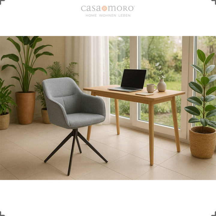 360° drehbarer Polsterstuhl mit Armlehnen in Grau an einem Holztisch mit Laptop, eingerahmt von Pflanzen und großen Fenstern in heller Wohnumgebung