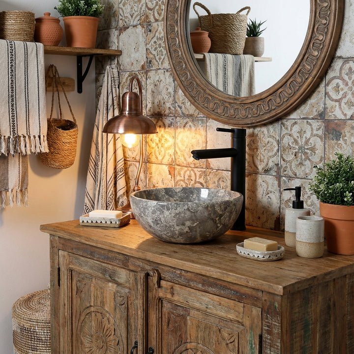 Lavabo redondo de mármol con grano gris sobre lavabo rústico de madera en un acogedor baño, combinado con accesorios negros, azulejos estampados e iluminación cálida