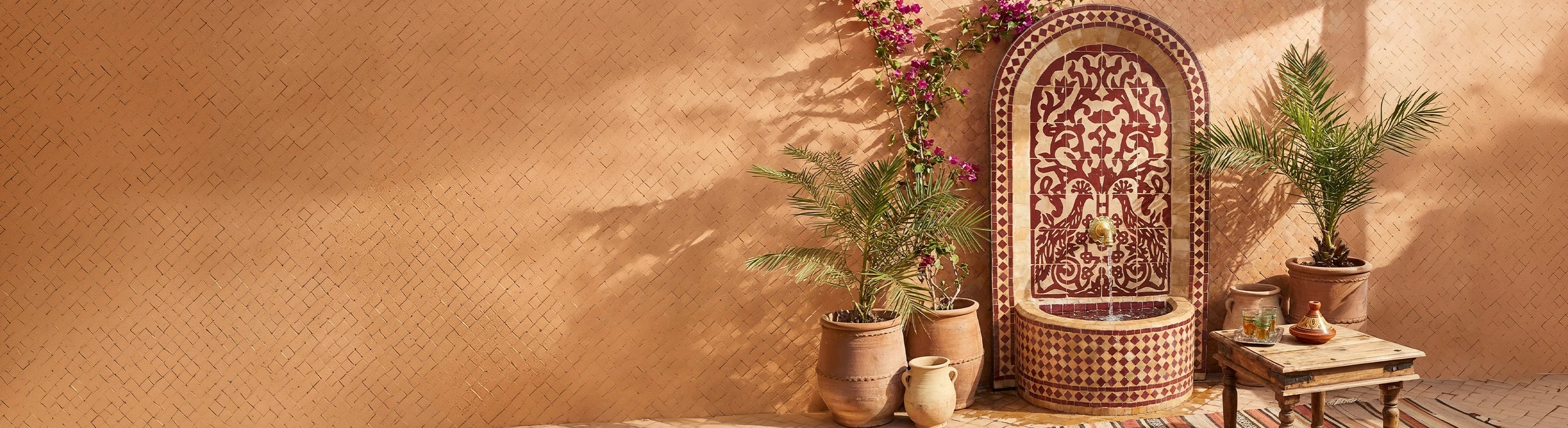fuente de mosaico – Marokkanischer Mosaikbrunnen mit Zellige-Fliesen als Wasserbrunnen im Garten vor warmer Wand mit Pflanzen und orientalischer Atmosphäre
