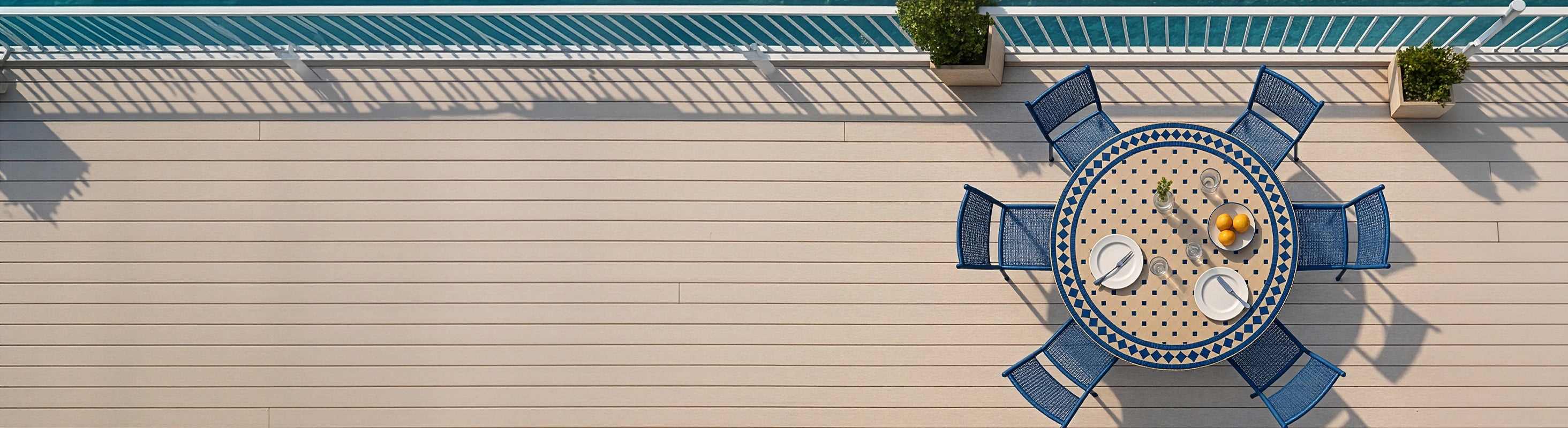 Mesas mosaico Ø120 – Gran mesa redonda de mosaico de Ø120 cm con azulejos de zellige azules y varias sillas a vista de pájaro en una terraza con vistas al mar
