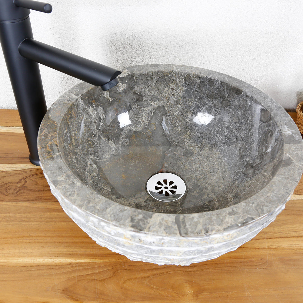 Lavabo sobre encimera redondo de piedra natural con superficie interior pulida y borde exterior estructurado sobre encimera de madera