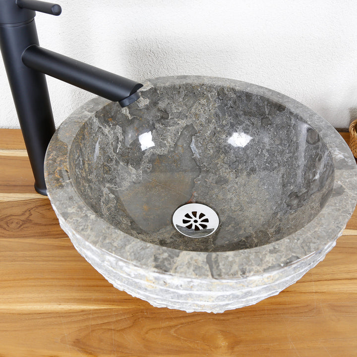 Lavabo sobre encimera redondo de piedra natural con superficie interior pulida y borde exterior estructurado sobre encimera de madera