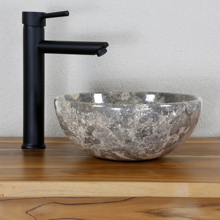 Lavabo sobre encimera redondo de piedra natural con vetas marrón grisáceo sobre encimera de madera, combinado con grifería independiente negra