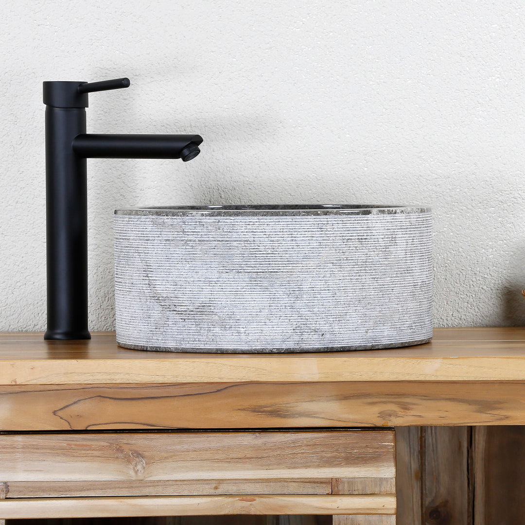 moderno Lavabo Realizada en piedra natural clara con una estructura de líneas finas y herrajes negros sobre una consola de madera.