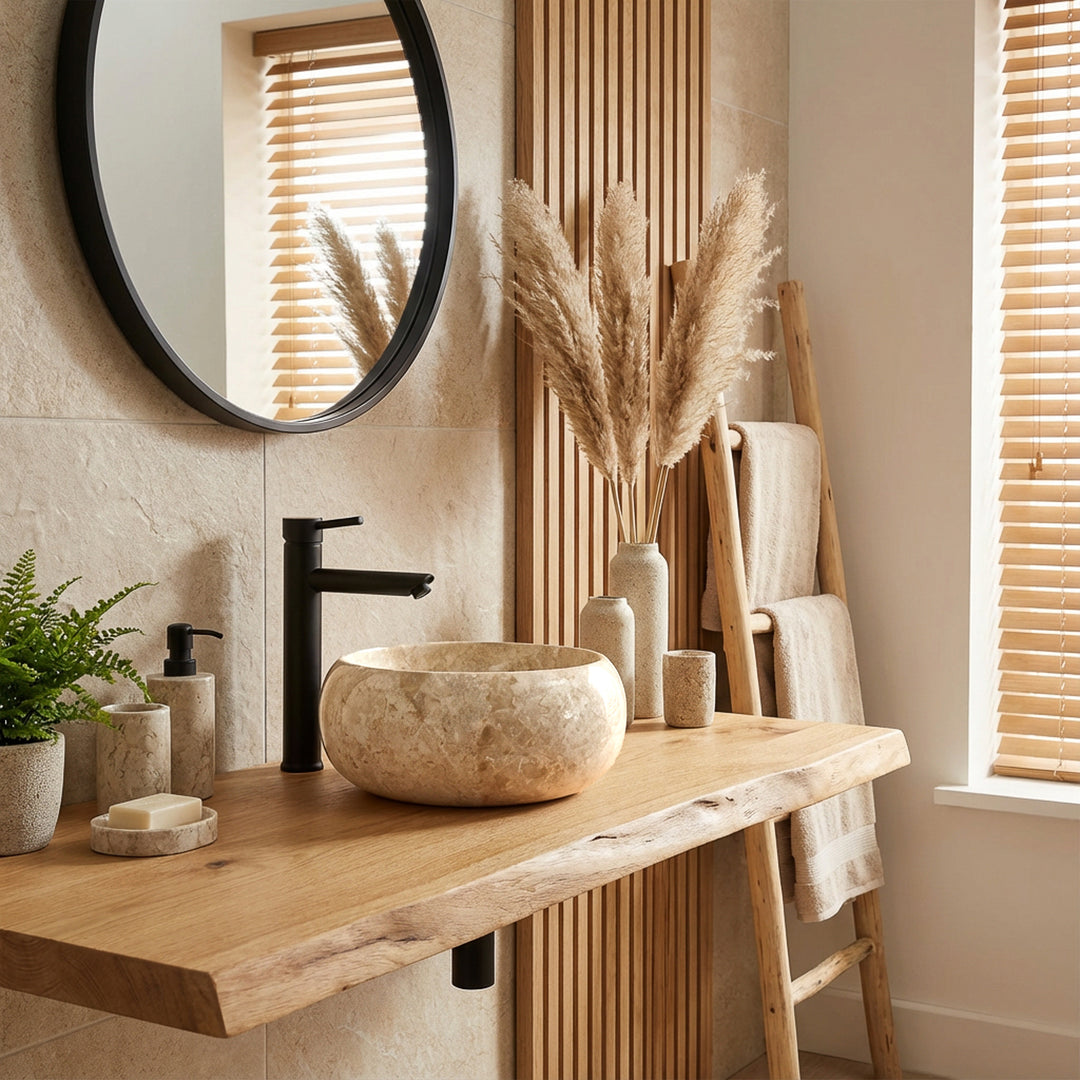 Lavabo sobre encimera redondo de piedra natural clara sobre un lavabo de madera con grifería negra en un ambiente de baño moderno y luminoso