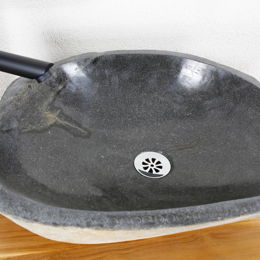 Vista detallada de un lavabo de piedra con una superficie interior finamente pulida, veta natural y desagüe central.