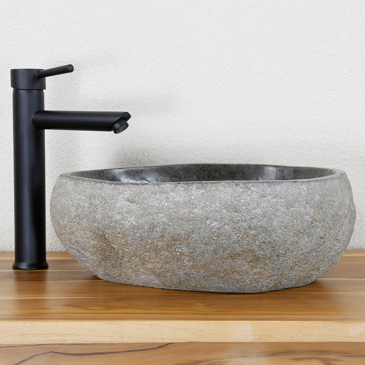 Lavabo Realizado en piedra natural gris de forma ovalada, combinado con herrajes negros sobre una cálida superficie de madera.