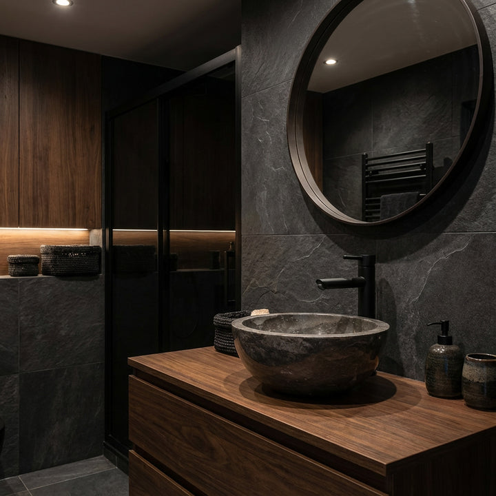 Rundes Naturstein-Waschbecken als Aufsatz auf dunklem Holzwaschtisch mit schwarzer Armatur im eleganten, dunklen Badambiente