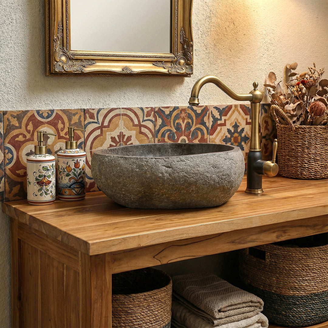 Lavabo de piedra natural en un cálido baño boho sobre tocador de madera, combinado con accesorios de latón y azulejos estampados