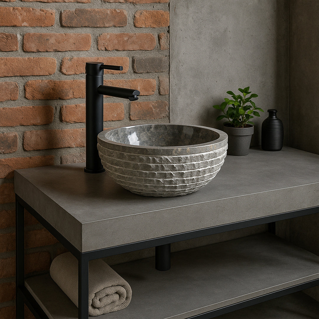 Lavabo de piedra gris como lavabo sobre encimera en un tocador de hormigón, baño moderno con paredes de ladrillo y accesorios negros