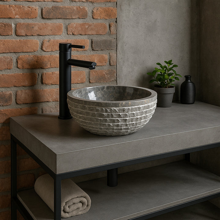 Lavabo de piedra gris como lavabo sobre encimera en un tocador de hormigón, baño moderno con paredes de ladrillo y accesorios negros