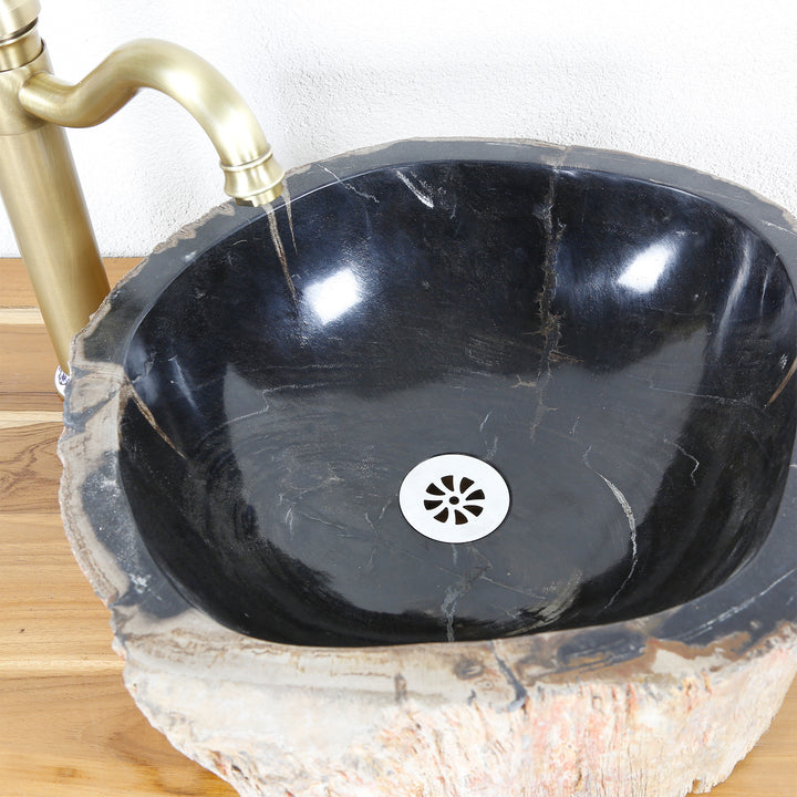 Fregadero de piedra de madera petrificada con superficie interior pulida oscura, vista superior con desagüe y accesorio de latón sobre tapa de madera.