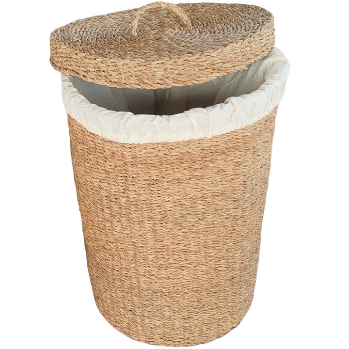 Cesta para la ropa trenzada de algas marinas con una capacidad de 75 litros, con un forro de tela clara y una tapa colocada en diagonal.