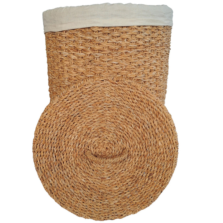 Cesto para la ropa de algas marinas de color natural, con un inserto de tela clara y una tapa colocada delante.