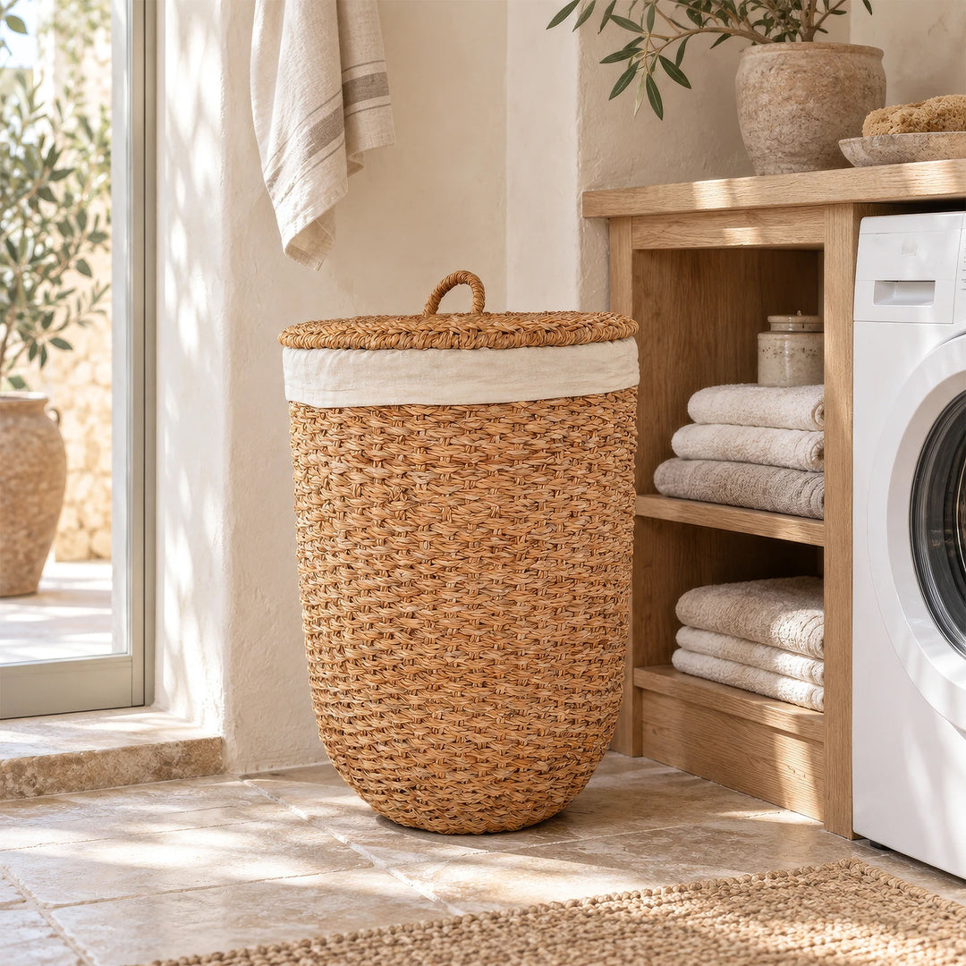 Cesto de la ropa con tapa, fabricado con algas marinas de color natural, junto a un estante para toallas y una lavadora en el lavadero.