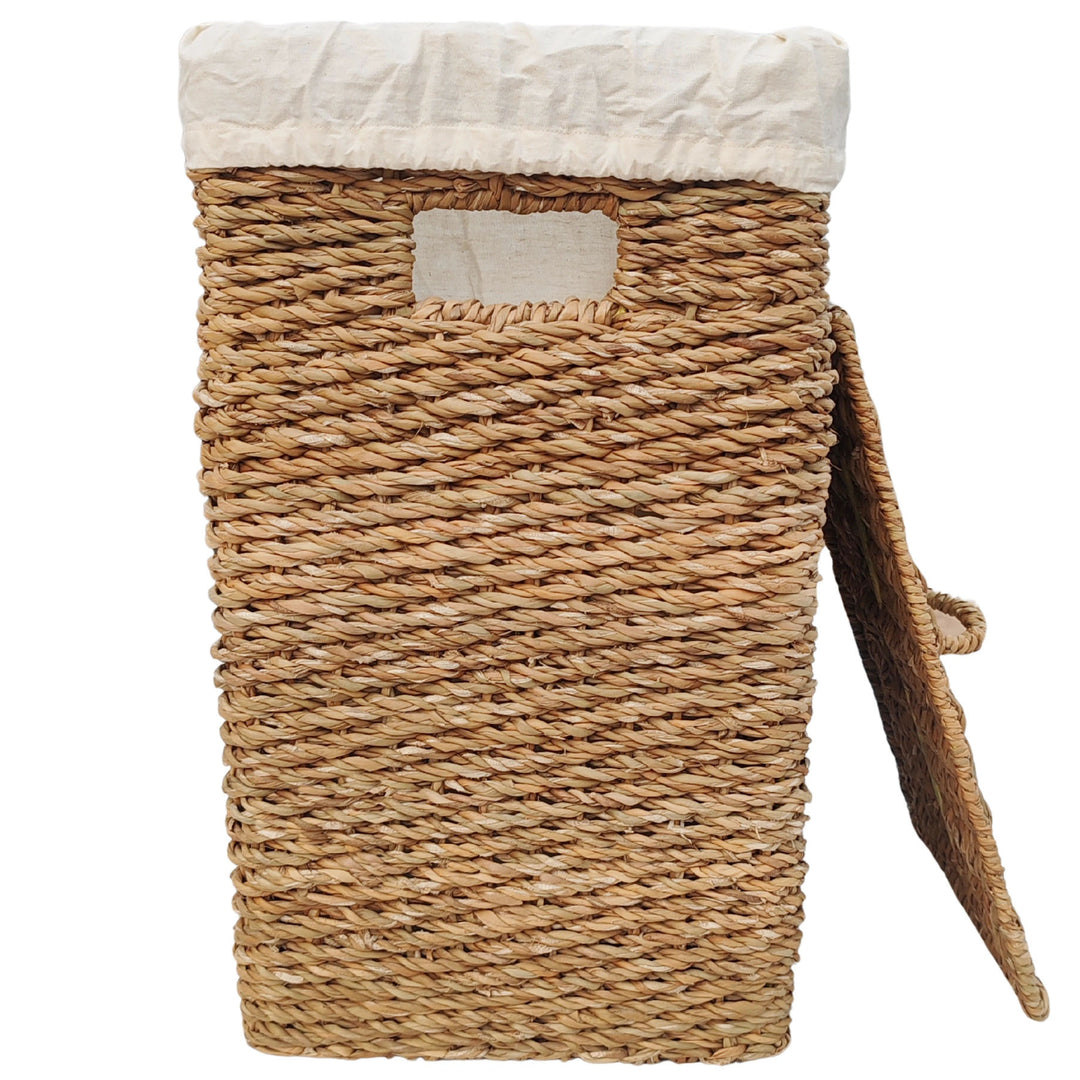 Cesto rectangular para la ropa sucia fabricado en algas marinas, con una capacidad de 50 litros, un inserto de tela clara y una tapa que se apoya lateralmente.