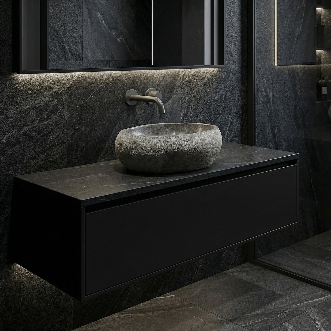 Lavabo hecho de piedra oscura en un baño moderno sobre un mueble de base flotante, con accesorios de pared e iluminación reducida