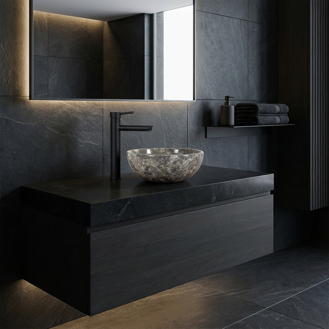 Lavabo sobre encimera redondo de piedra natural con vetas de color marrón grisáceo sobre un lavabo oscuro en el baño moderno, combinado con accesorios negros y diseño de pared oscura