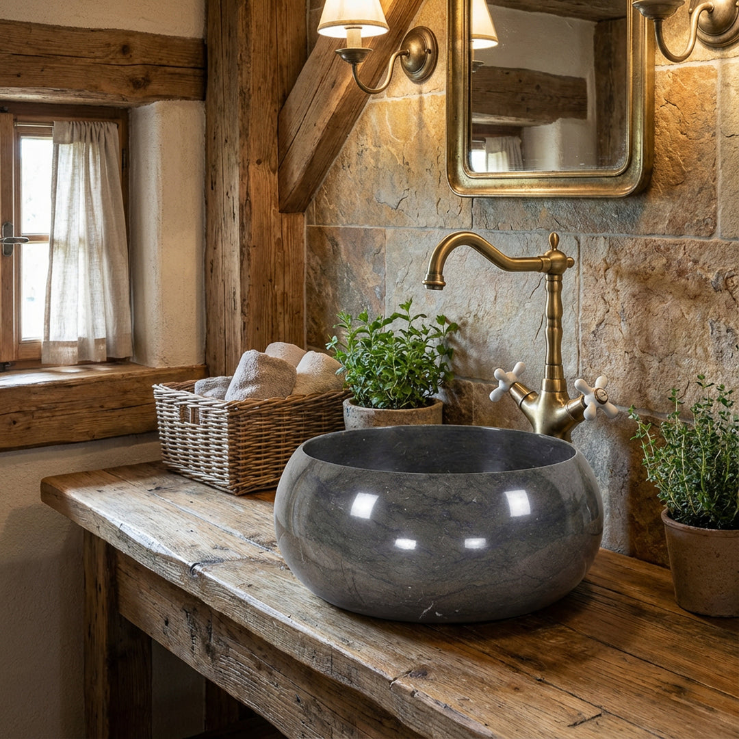 Lavabo redondo de piedra natural sobre una mesa rústica de madera en un acogedor baño con accesorios de latón y luz cálida