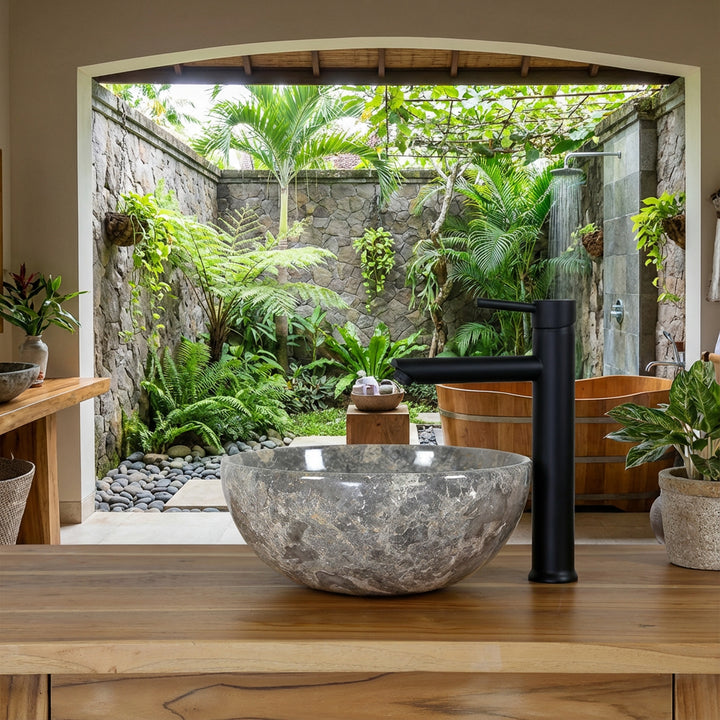 piedra natural redonda Lavabo con vetas de color marrón grisáceo sobre un lavabo de madera en el baño spa abierto con vistas a un patio verde, combinado con una grifería independiente negra, una pared de piedra natural y una bañera de madera