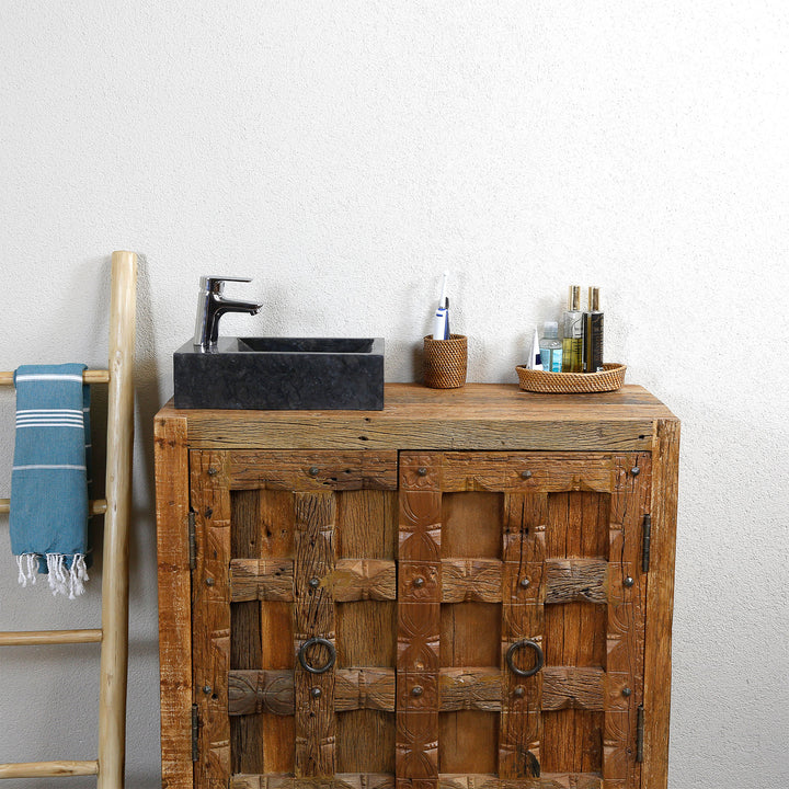 Lavabo sobre encimera cuadrado de mármol con vetas oscuras sobre un lavabo rústico de madera, combinado con grifería cromada y accesorios naturales frente a una pared clara