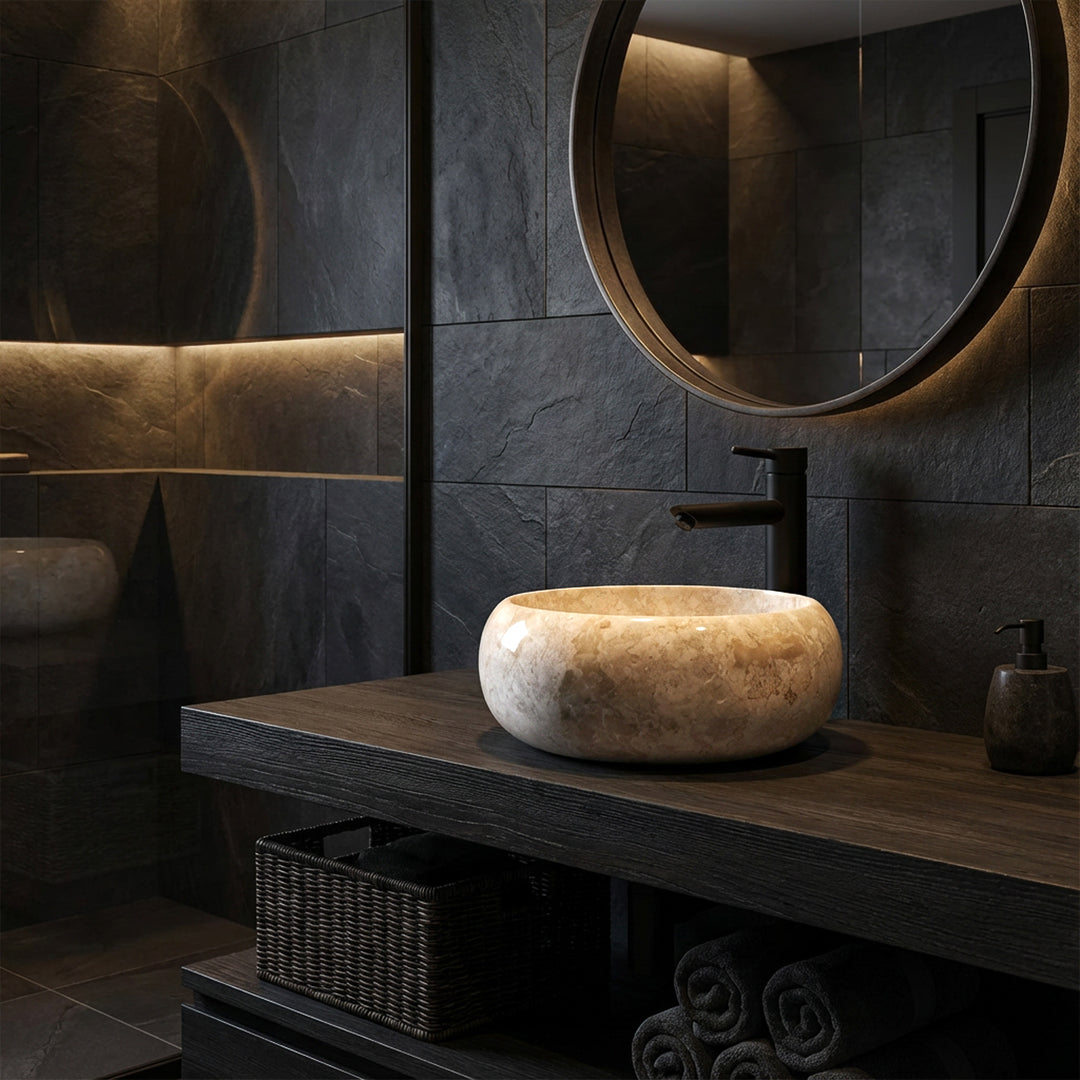 Lavabo sobre encimera redondo de piedra natural sobre un lavabo de madera oscura con accesorios negros en un ambiente de baño moderno y oscuro