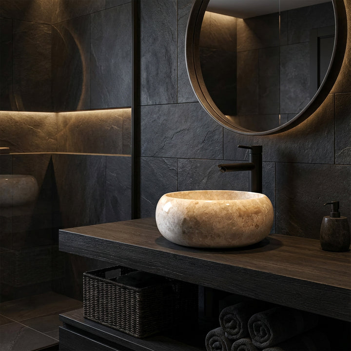Lavabo sobre encimera redondo de piedra natural sobre un lavabo de madera oscura con accesorios negros en un ambiente de baño moderno y oscuro