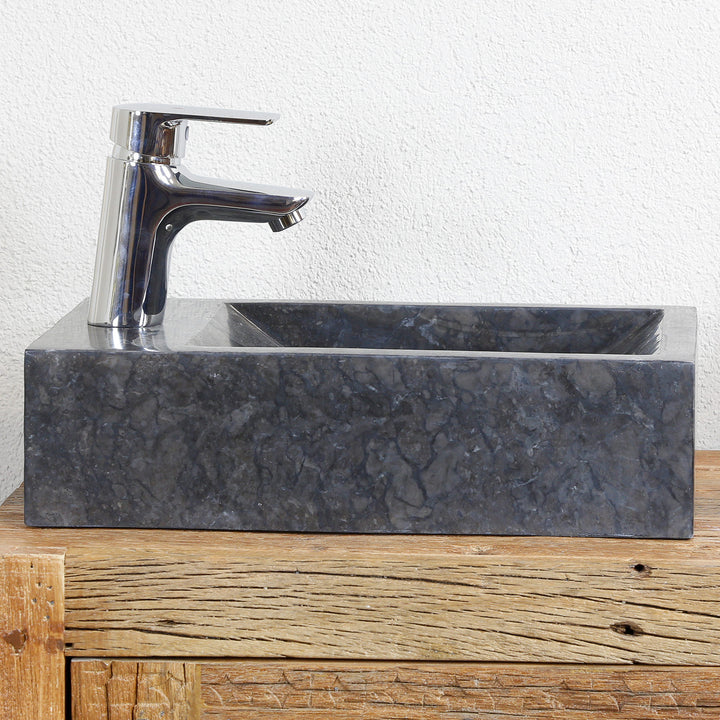 Lavabo sobre encimera cuadrado de mármol con vetas oscuras sobre una consola de madera, combinado con herrajes cromados frente a una pared clara